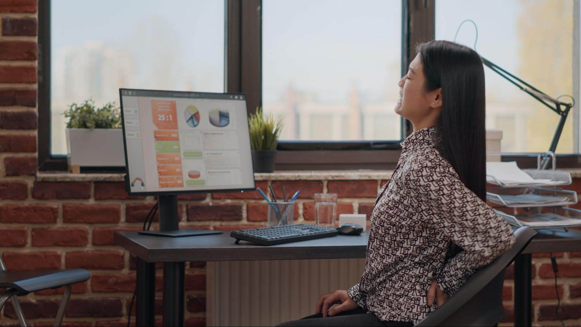 kobieta siedząca przy biurku i cierpiąca z powodu bólu pleców